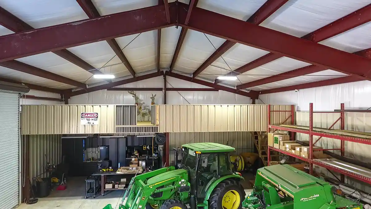 Green tractor with front loader parked inside a workshop near a tool bench and storage shelves